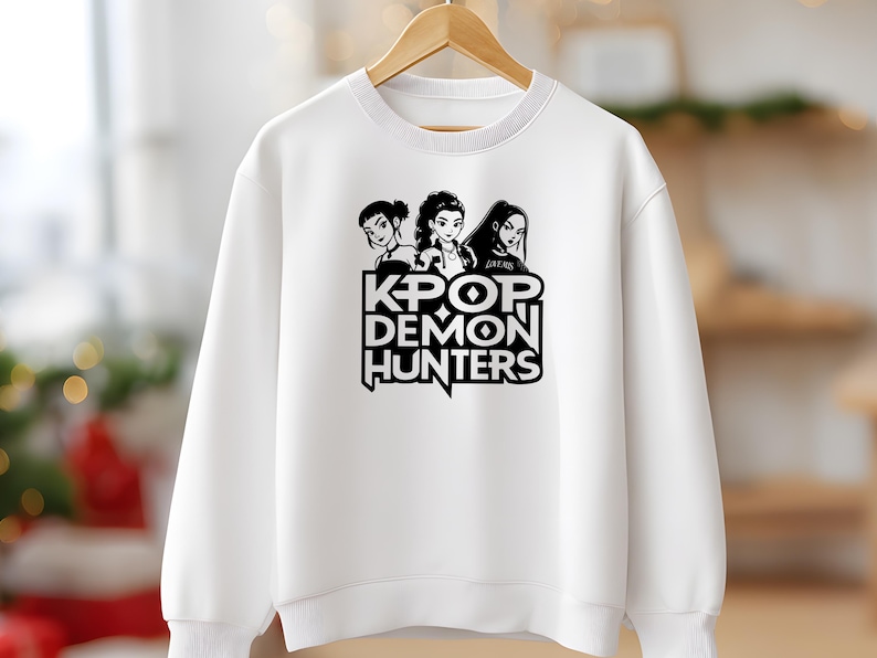 May include: White sweatshirt featuring a black and white graphic of three stylized female figures above the text "KPOP DEMON HUNTERS". The design is centered on the front of the crew neck sweatshirt.