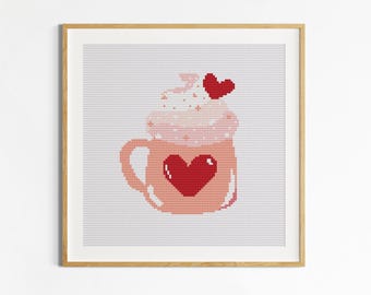May include: Cross-stitch pattern of a pink mug with a red heart, topped with whipped cream and a small red heart. The image is framed in a wooden frame. The text "Etamine Patterns" is at the bottom.