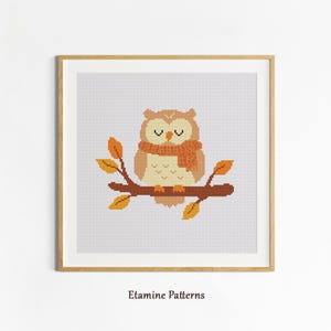 May include: Cross-stitch design featuring a cartoon owl with a scarf, sitting on a branch with autumn leaves. The owl is in shades of brown and orange, with closed eyes. The artwork is framed in a wooden frame, with the text "Etamine Patterns" at the bottom.