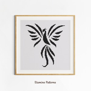 May include: A framed cross-stitch pattern with a black phoenix design on a white background. The phoenix has outstretched wings and flowing tail feathers. The frame is light brown. The text "Etamine Patterns" is at the bottom of the image.