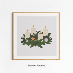 May include: Cross-stitch art of an Advent wreath with four white candles, green foliage, and a gold star. The artwork is framed in a light wood frame. The text "Etamine Patterns" is at the bottom of the image.