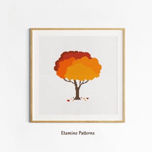 Könnte beinhalten: Gerahmtes Kreuzstich-Kunstwerk mit einem pixeligen Baum mit braunem Stamm und einer geschichteten Krone aus orangefarbenen und roten Blättern. Das Kunstwerk ist vor einem weißen Hintergrund platziert und in einem hellen Holzrahmen gerahmt. Der Text "Etamine Patterns" befindet sich unten.
