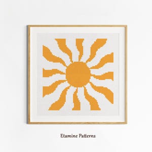 May include: Framed cross-stitch art depicting a stylized sun in orange and white. The sun has a circular centre with radiating wavy lines. The artwork is displayed in a wooden frame. The text "Etamine Patterns" is at the bottom.