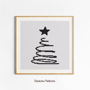 May include: A framed cross-stitch artwork in black and white, depicting a minimalist Christmas tree with a star at the top. The design is set against a white backdrop and enclosed in a light brown wooden frame. The text "Etamine Patterns" is at the bottom.
