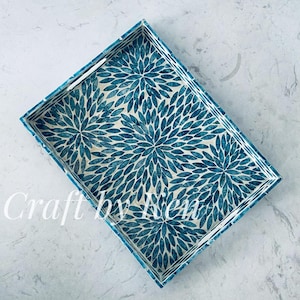 Puede incluir: Una bandeja rectangular con un patrón floral azul y blanco. La bandeja tiene un borde elevado y dos asas a los lados.