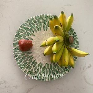 May include: A green and white mosaic serving tray with a bunch of yellow bananas and a red fruit on top. The tray has a leaf pattern and the text "Craft by Ren" is visible at the bottom.