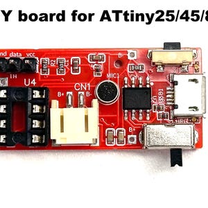 May include: A red DIY board for ATtiny25/45/85 microcontrollers. The board features various components, including connectors, a microphone, and a USB port. Text on the board includes "gnd data vcc", "U4", "CN1", and "MIC1".