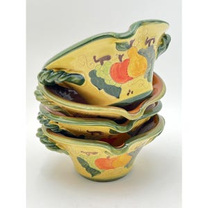 Puede incluir: Un juego de cuatro cuencos de cerámica amarilla con detalles pintados en verde y marrón. Los cuencos presentan un diseño de frutas con peras, uvas y manzanas. Los cuencos tienen un borde ondulado único y un asa a cada lado.