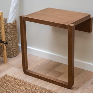 Dark birch plywood folding wall chair unfolded for seating, minimalist and space-saving design.