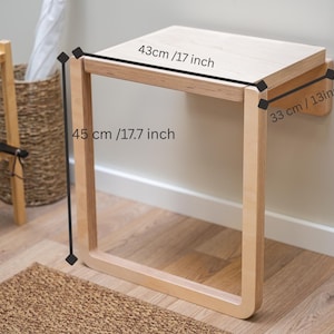 May include: A light-colored wooden wall-mounted bench. The bench is 17 inches wide, 17.7 inches high, and 13 inches deep. The bench has a simple, modern design and is mounted on a white wall. The bench is in a room with a wooden floor.