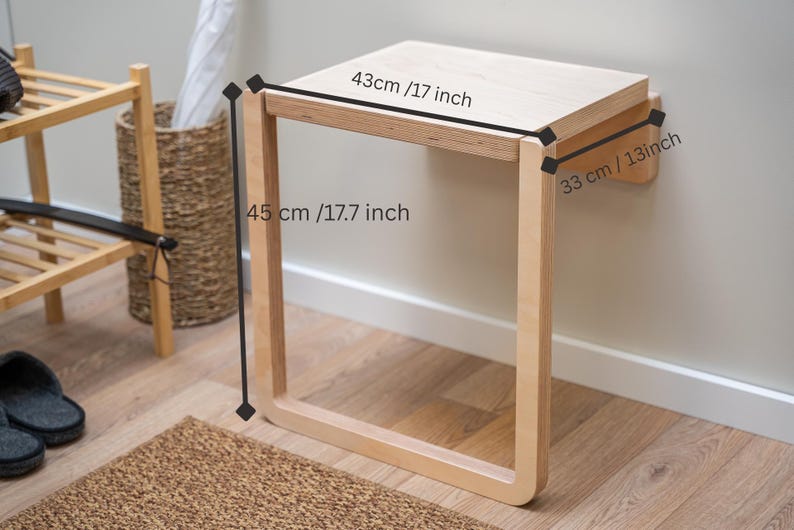 May include: A light-colored wooden wall-mounted bench. The bench is 17 inches wide, 17.7 inches high, and 13 inches deep. The bench has a simple, modern design and is mounted on a white wall. The bench is in a room with a wooden floor.