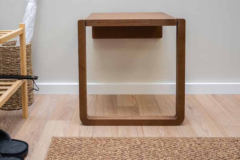 Puede incluir: Una mesa auxiliar de madera de forma cuadrada con un acabado marr&oacute;n c&aacute;lido. La mesa tiene un dise&ntilde;o minimalista con una parte superior rectangular y una base de marco abierto. La mesa mide aproximadamente 61 cm de alto y est&aacute; sobre un suelo de madera.