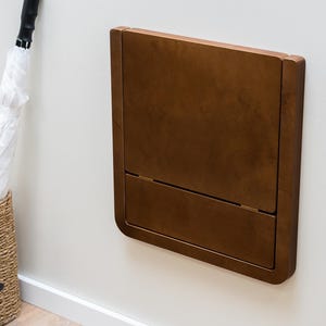 Dark walnut-stained birch plywood folding wall chair folded neatly against wall for a modern interior look.