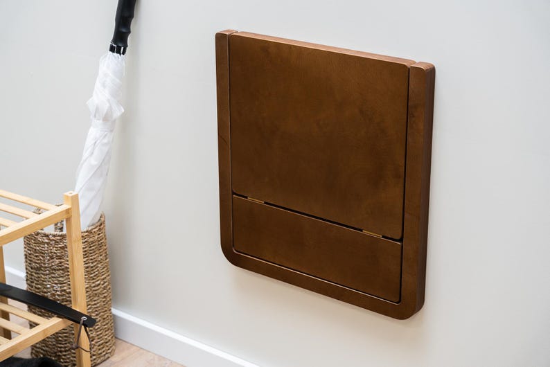 Dark walnut-stained birch plywood folding wall chair folded neatly against wall for a modern interior look.