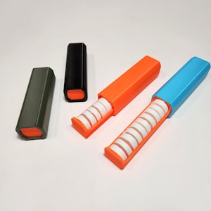 以下が含まれることがあります： カラフルな長方形の容器のコレクション。一部は開いており、白い円筒形の物体が明らかになっています。容器は緑、黒、オレンジ、青の色合いです。内部のオブジェクトは、紙のロールまたは同様のもののようです。