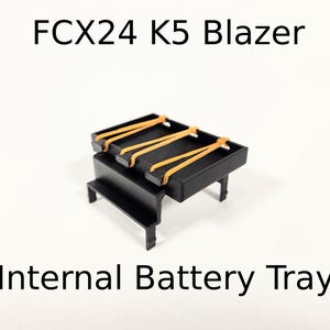 以下が含まれることがあります： FCX24 K5 ブレイザー用の、オレンジ色のゴム製ストラップが付いた黒いプラスチック製の内部バッテリートレイです。