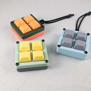 May include: Three small, square keychains with four buttons each. The keychains are made of plastic and have different colored buttons. One keychain has orange buttons, one has yellow buttons, and one has gray buttons.