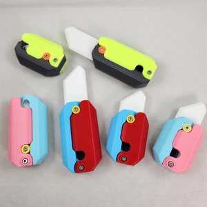 May include: Five small, colorful, multi-colored, pocket-sized utility knives with white blades. The knives are made of plastic and have a variety of colors, including pink, blue, red, yellow, and black.