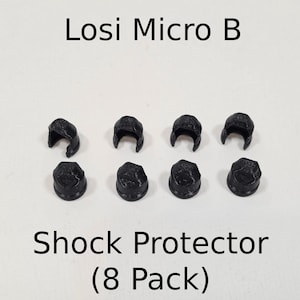 May include: Eight black Losi Micro B shock protectors arranged in two rows of four. The top row shows four open-ended clips, while the bottom row displays four solid, cap-like protectors. The text Losi Micro B Shock Protector (8 Pack) is visible.