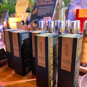 Puede incluir: Cuatro botellas negras de aceite sagrado de Palo Santo para masaje y cuerpo, con letras doradas y un c&oacute;digo QR en la etiqueta. Las botellas est&aacute;n dispuestas en fila sobre una superficie de madera. Las botellas est&aacute;n etiquetadas con "purism" y "Palo Santo sacred oil".