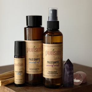 Puede incluir: Tres botellas de vidrio marr&oacute;n con etiquetas que dicen "purism" y "Palo Santo" en varios tama&ntilde;os. Las botellas contienen aceite sagrado de Palo Santo, bruma sagrada y aceite de rodillo. Las botellas est&aacute;n dispuestas sobre una superficie de madera con palitos de incienso de Palo Santo y un cristal morado.