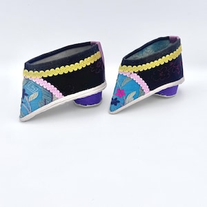 May include: A pair of antique Chinese lotus shoes. The shoes feature a black upper with floral embroidery in blue and pink, accented with yellow and pink trim. The heels are a solid purple color.