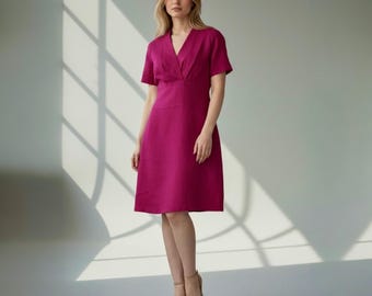 May include: A magenta-colored dress with a V-neckline and short sleeves. The dress has a fitted bodice and a knee-length skirt. The model is wearing nude-colored heels. The background is a plain white wall with shadows.