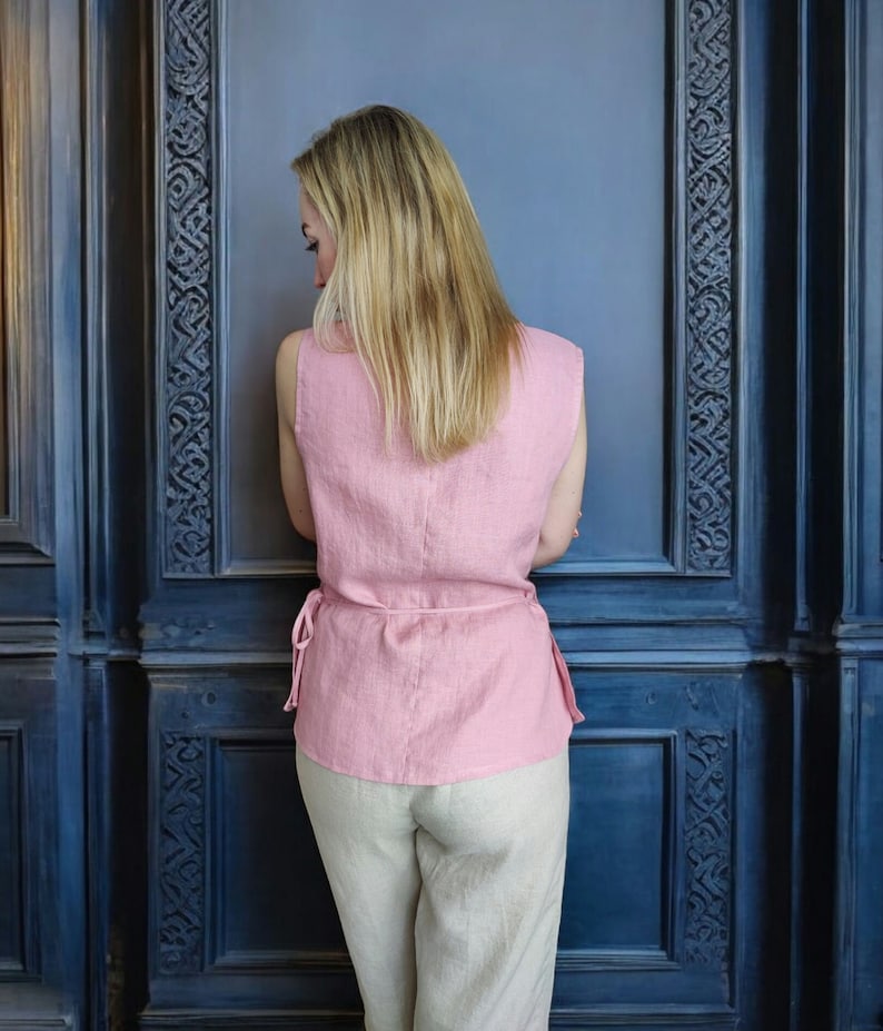 Pode incluir: Uma mulher vestindo uma blusa de linho rosa sem mangas com cintura amarrada e cal&ccedil;as de linho bege. A blusa tem um caimento solto e um comprimento ligeiramente curto. As cal&ccedil;as s&atilde;o de perna reta e t&ecirc;m cintura alta.