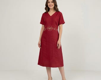 May include: A red V-neck dress with short sleeves and a floral embroidered design at the waist. The dress falls to the mid-calf and is paired with beige heels. The dress is made of a lightweight fabric.