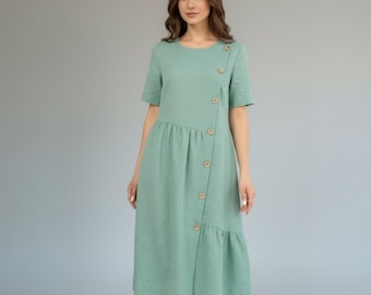 May include: A light green linen dress with short sleeves and a button-up front. The dress features a round neckline, a gathered waist, and a ruffled hem. The buttons are a light brown color.