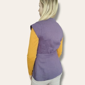 Pode incluir: Um colete roxo sem mangas com cinto, usado sobre uma camisa amarela de manga comprida.