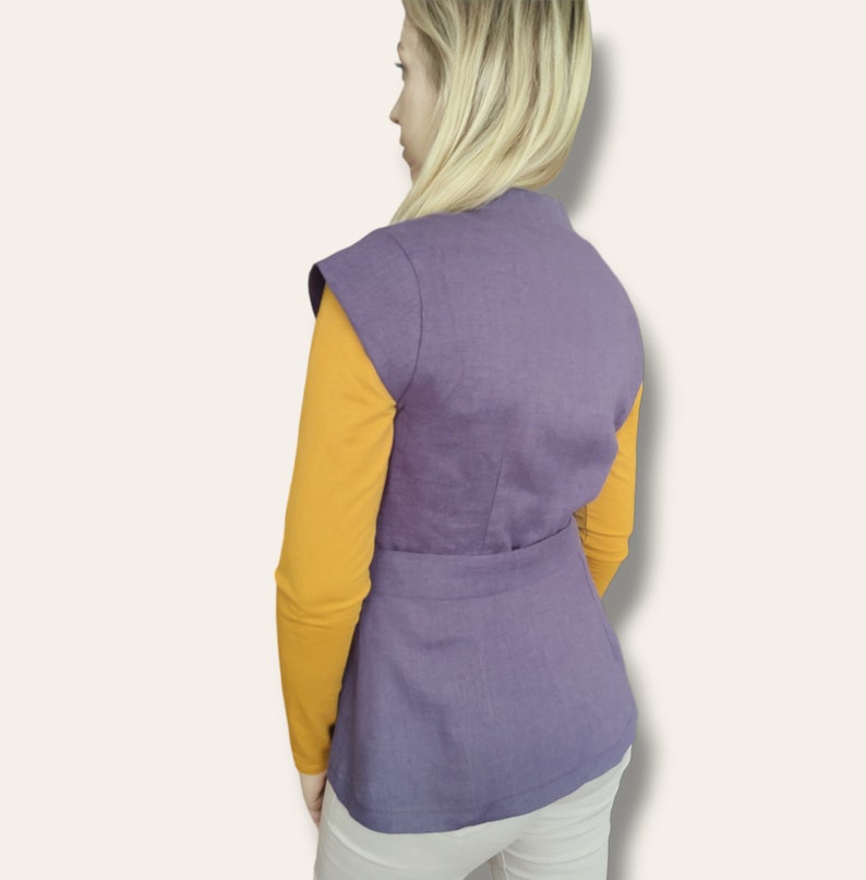 Pode incluir: Um colete roxo sem mangas com cinto, usado sobre uma camisa amarela de manga comprida.