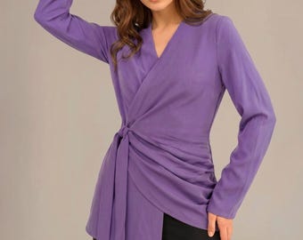 May include: A long-sleeved wrap blouse in a solid purple hue, featuring a V-neckline and a side-tie closure that creates gathered, draped fabric across the front. The garment is paired with plain black trousers, completing the ensemble.