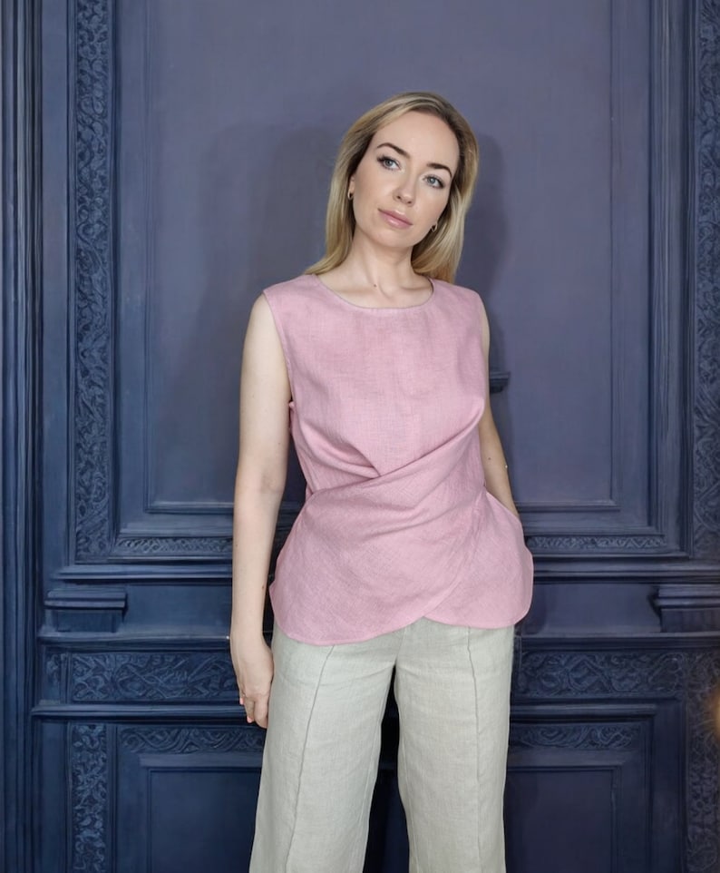 Pode incluir: Uma mulher vestindo uma blusa de linho rosa com um detalhe de n&oacute; e cal&ccedil;as de linho bege. A blusa tem um decote redondo e &eacute; sem mangas.