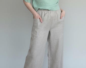 May include: A light green linen top with a keyhole neckline and short sleeves paired with light beige linen wide-leg pants. The pants have pockets and an elastic waistband. The outfit is made of a lightweight fabric.