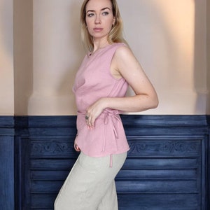 Pode incluir: Uma blusa rosa sem mangas com um la&ccedil;o na cintura. A blusa &eacute; feita de um tecido macio e fluido e tem um caimento solto. A modelo est&aacute; usando a blusa com cal&ccedil;as bege.