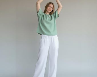May include: A person wearing a mint green short-sleeve top and white wide-leg pants. The top has a round neckline and a keyhole detail. The pants have pockets. The outfit is made of a lightweight fabric.