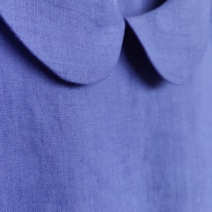May include: A close-up of a blue linen shirt with a Peter Pan collar. The fabric has a textured weave.