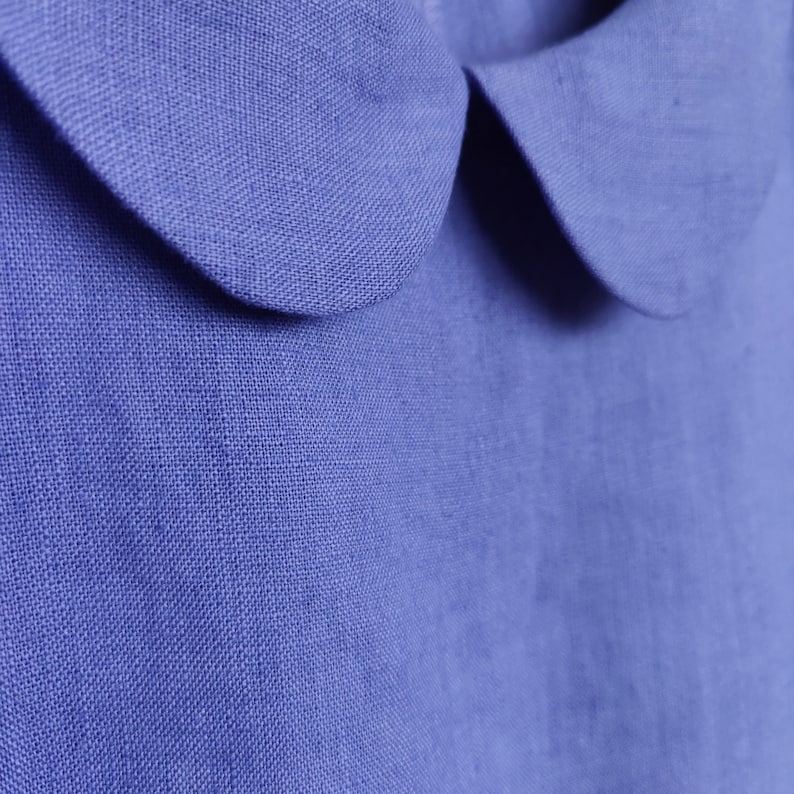 May include: A close-up of a blue linen shirt with a Peter Pan collar. The fabric has a textured weave.