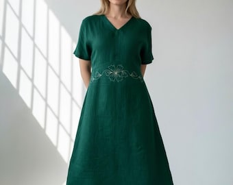 May include: A dark green linen dress with a V-neck and short sleeves. The dress features a floral embroidery design across the waistline. The dress has a midi length.