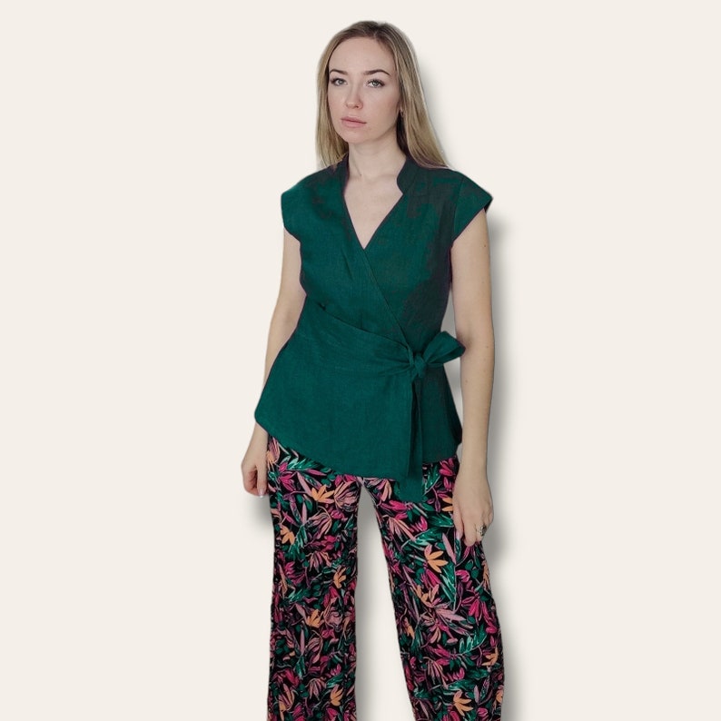 Pode incluir: Um top verde escuro estilo envelope com decote em V e mangas curtas. O top tem um la&ccedil;o na cintura e &eacute; usado com cal&ccedil;as de estampa floral.