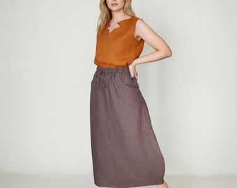 May include: A sleeveless, burnt orange top with a unique neckline paired with a long, dark brown skirt. The skirt has a drawstring waist and pockets. The outfit is made of a soft, flowing fabric, perfect for a casual, yet stylish look.