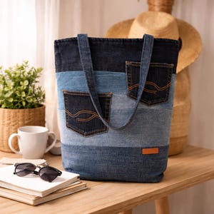 Könnte beinhalten: Eine Denim-Tragetasche mit Patchwork-Design in verschiedenen Blautönen. Die Tasche hat zwei Vordertaschen mit orangefarbenen Nähten und ein kleines braunes Lederetikett. Die Griffe bestehen aus dem gleichen Denim-Material.