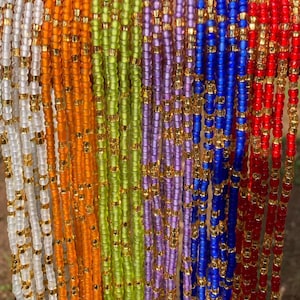 May include: A collection of colorful beaded waist beads with gold accents. The beads are strung on a thin cord and are available in a variety of colors, including white, orange, green, purple, blue, and red.