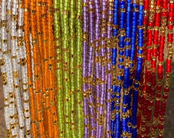 Puede incluir: Una colección de cuentas de cintura de colores con detalles dorados. Las cuentas están enhebradas en un cordón delgado y están disponibles en una variedad de colores, incluyendo blanco, naranja, verde, morado, azul y rojo.