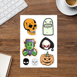 May include: A sheet of Halloween stickers with cartoon illustrations. The stickers depict an orange skull, a green ghost, Frankenstein's monster, a grim reaper, a jack-o'-lantern, and two additional skulls.