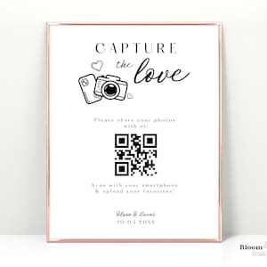 May include: A white sign with a black border and a rose gold frame. The sign says "Capture the love" with a camera and hearts. It also has a QR code and the text "Please share your photos with us! Scan with your smartphone & upload your favorites! Olivia & Lucas 10.05.20NN"