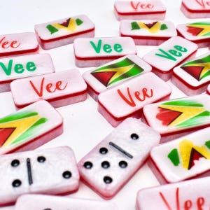 May include: A collection of pink dominoes with red borders and the word "Vee" in green or red script. Some dominoes feature a flag design with yellow, green, red, and black colors. One domino shows black dots.