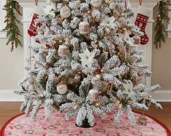 Könnte beinhalten: Ein geschmückter Weihnachtsbaum mit weißen Ornamenten, Lichtern und einem rosa Baumrock mit einem Weihnachtsmuster. Der Baumrock hat eine rote Bommelborte. Der Baum steht vor einem Kamin mit Strümpfen.