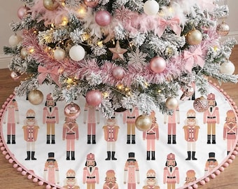 Könnte beinhalten: Ein geschmückter Weihnachtsbaum mit rosa und goldenen Ornamenten, Schleifen und einem Stern. Der Baumrock zeigt ein sich wiederholendes Muster aus rosa und beigen Nussknackerfiguren auf weißem Grund, gesäumt von rosa Pompons.